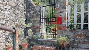 A stone wall with a metal gate, potted plants, and a brick pathway. - Villa lardarina (Corniglia Liguria)