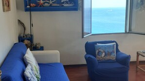 A room with a bed, a blue armchair, a small table, and a shelf with nautical decorations. - Villa lardarina (Corniglia Liguria)
