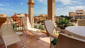 A terrace with white chairs and a table, overlooking a cityscape with buildings and palm trees.