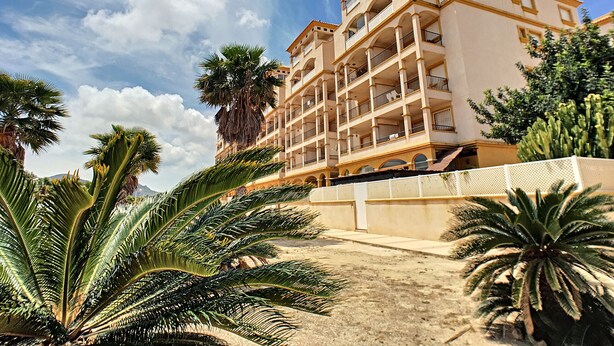 A multi-story hotel with balconies, palm trees, and a clear sky.