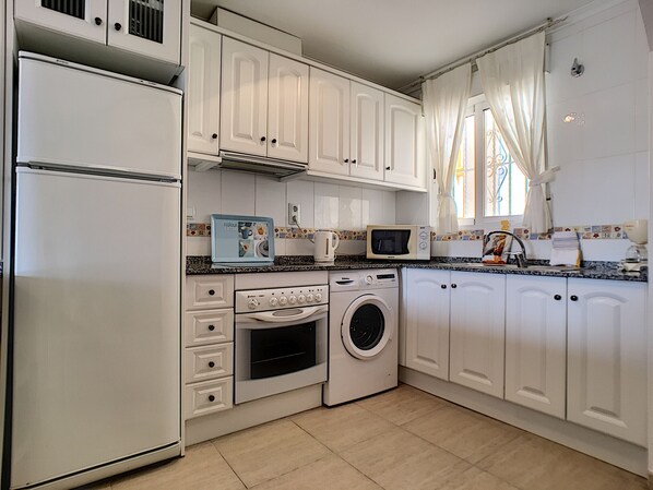 A kitchen with white cabinets, a microwave, a washing machine, and a refrigerator.
