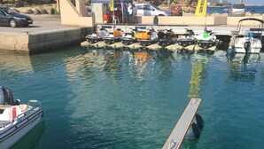 Ein Yachthafen mit vertäuten Booten, ein überdachter Bereich mit Menschen und freie Sicht auf das Wasser.