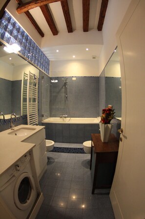 Un baño moderno con lavamanos, inodoro y bañera. Hay un espejo sobre el lavamanos y un techo con vigas de madera.