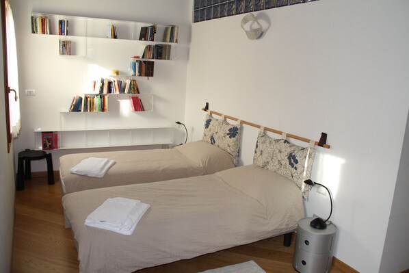 A bedroom with two beds, a bookshelf, and a bedside table with a lamp.
