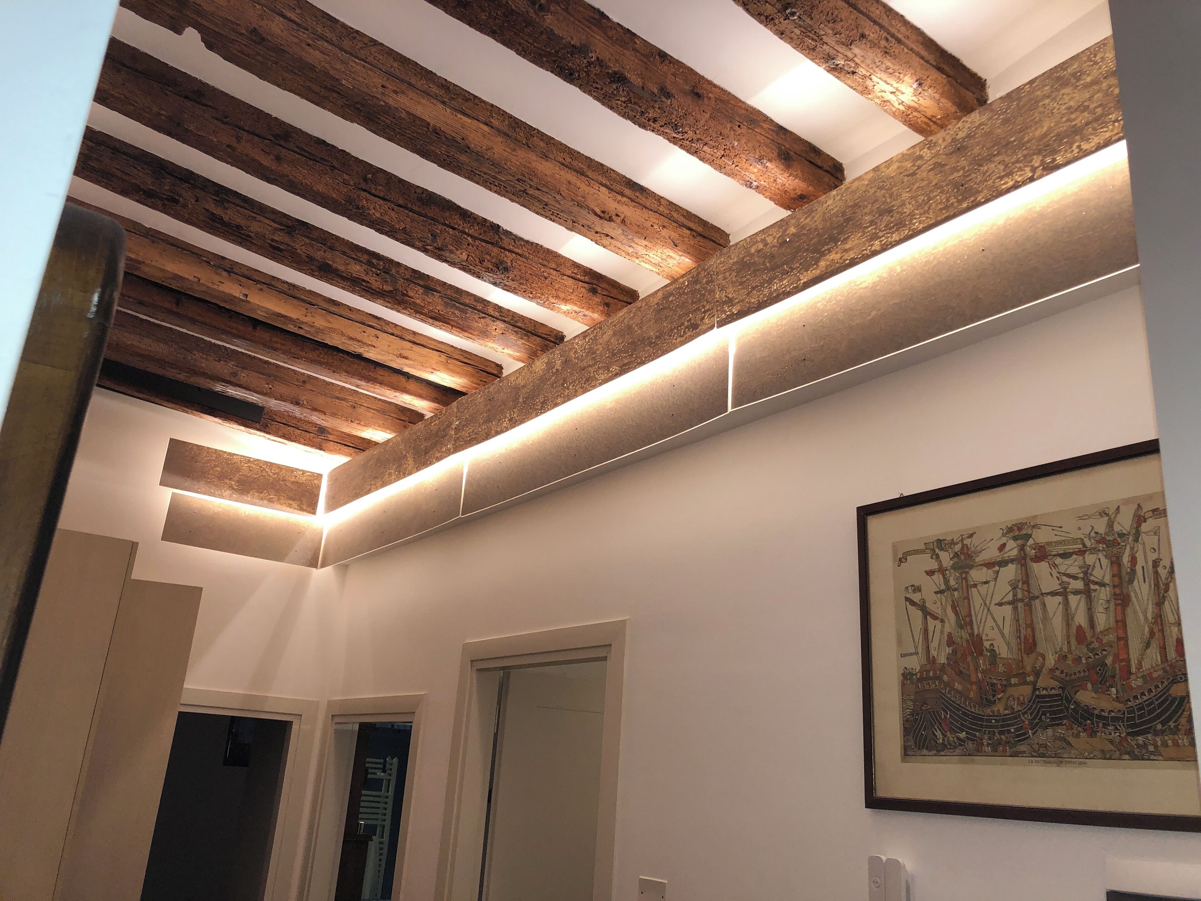 Un corridoio con travi a vista in legno, illuminazione incassata e un quadro appeso al muro.