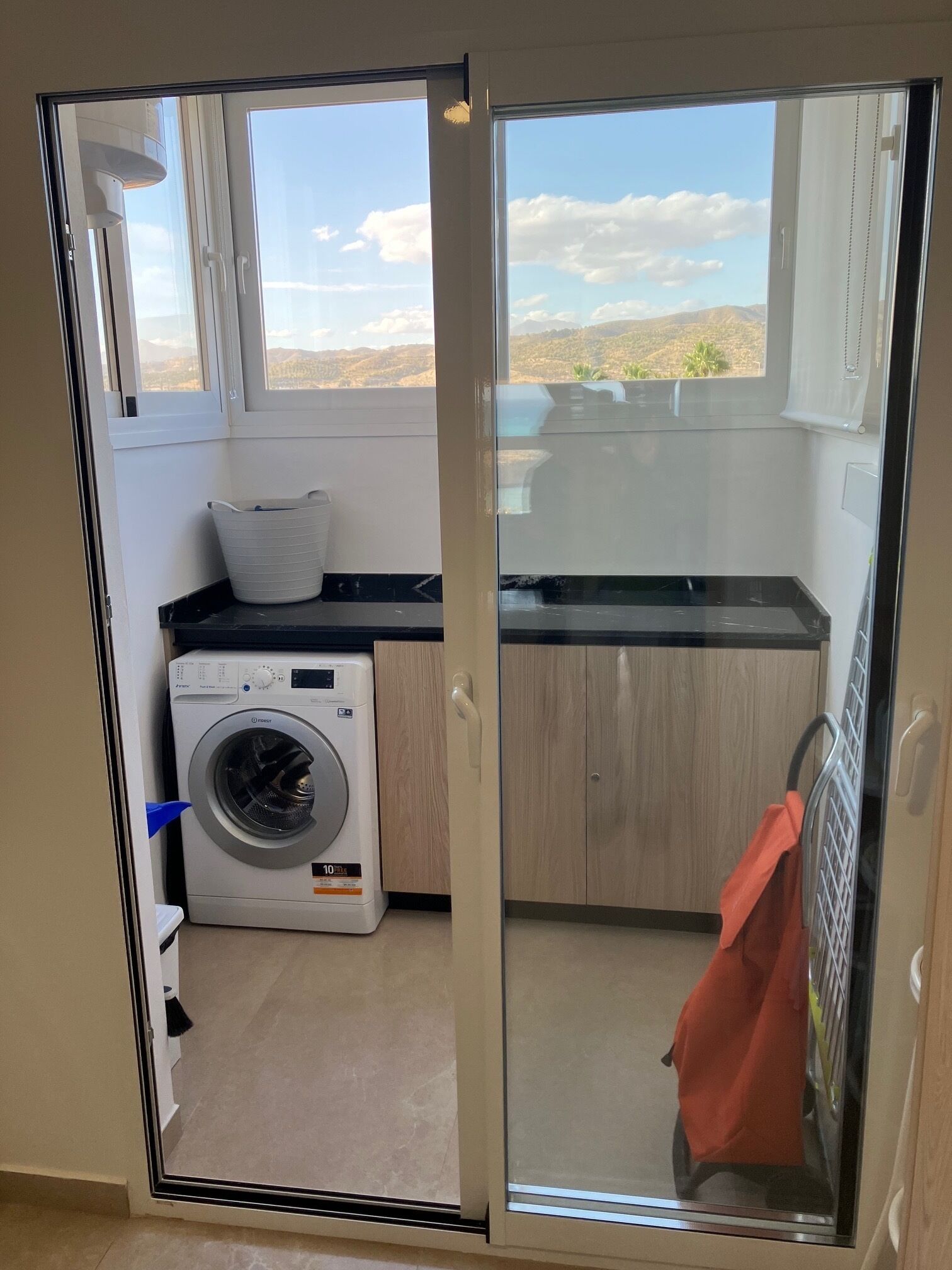 A laundry room with a washing machine, a drying rack, and a view of the outdoors.