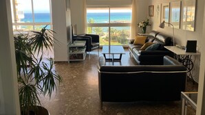 A spacious living room with a large window offering a view of the ocean, a ceiling fan, and a black leather sofa. - Apartment/ flat - El Campello (El Campello)