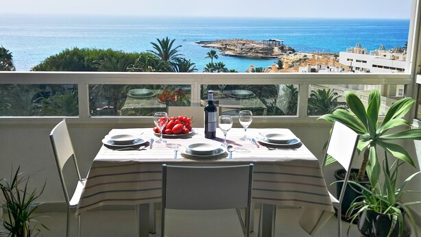 A balcony table set with plates, glasses, and a bottle, overlooking a coastal view with buildings and greenery. - Apartment/ flat - El Campello (El Campello)