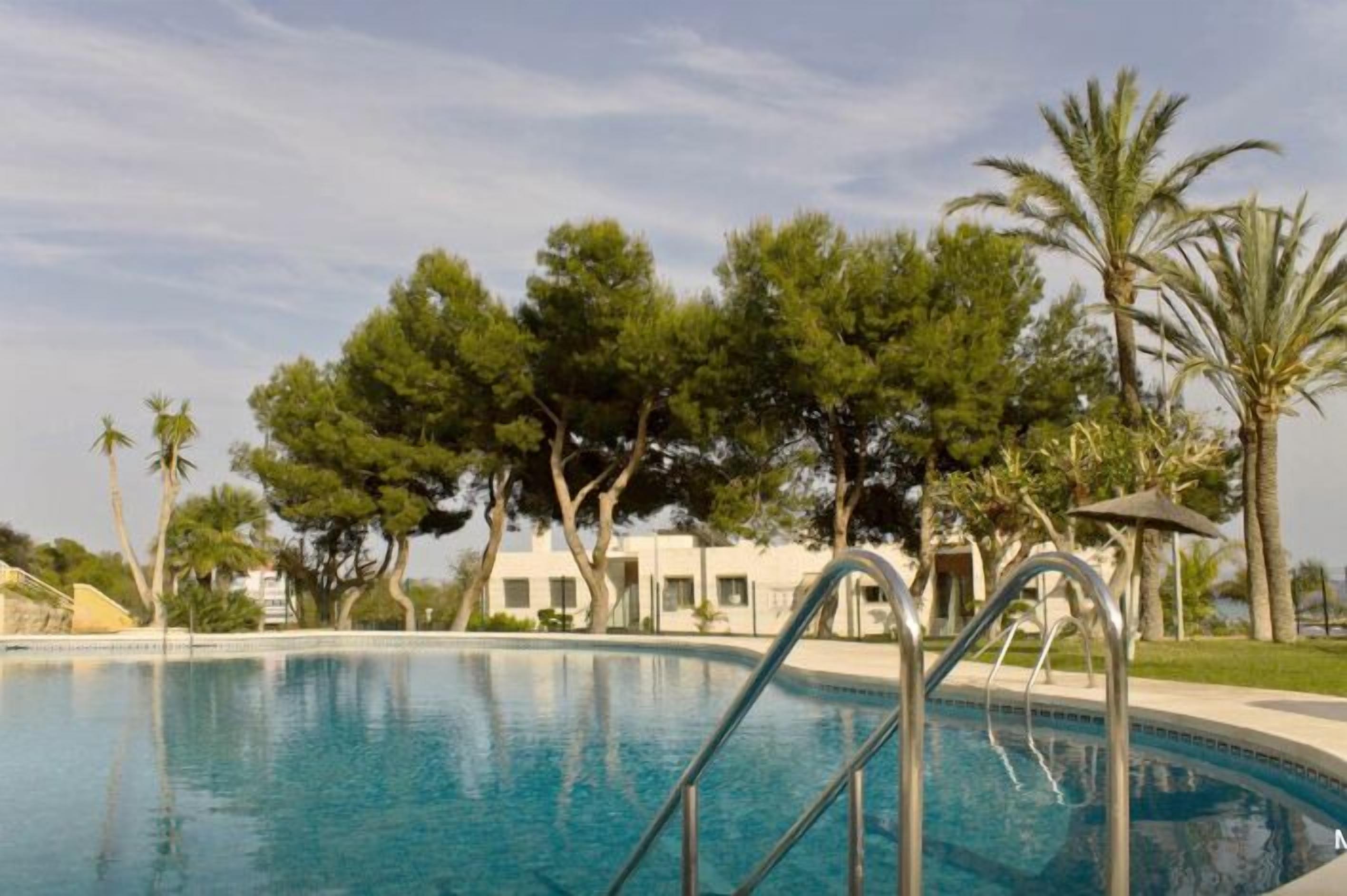A swimming pool with metal railings, surrounded by trees and a building in the background.