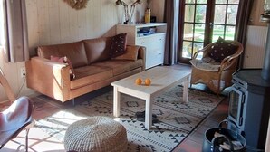 A cozy living room with a wooden ceiling, a brown leather sofa, a white coffee table, and a black stove.