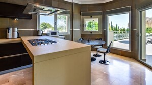 Een moderne keuken met een centraal eiland, geïntegreerde apparatuur en grote ramen met uitzicht op de omgeving.
