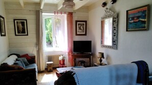 Een woonkamer met een bank, een televisie, een bijzettafeltje en een potplant.