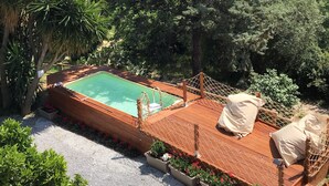 A wooden deck with a pool, surrounded by lush greenery and trees.