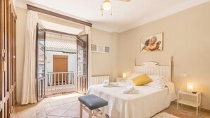 Ein Schlafzimmer mit Bett, Nachttisch, Bank, einem Balkon mit Geländer und einem Fenster mit Vorhängen.