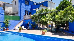 Ein Poolbereich mit blau gefliestem Pool, Sitzgelegenheiten im Freien und einer Treppe zu einem Gebäude mit blauen Wänden.