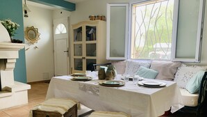 Un coin repas avec une table dressée pour quatre personnes, un meuble avec des portes en verre et une fenêtre donnant sur un paysage verdoyant.