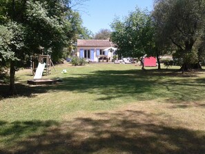 A grassy yard with a swing set, a small shed, and a house with a tiled roof.