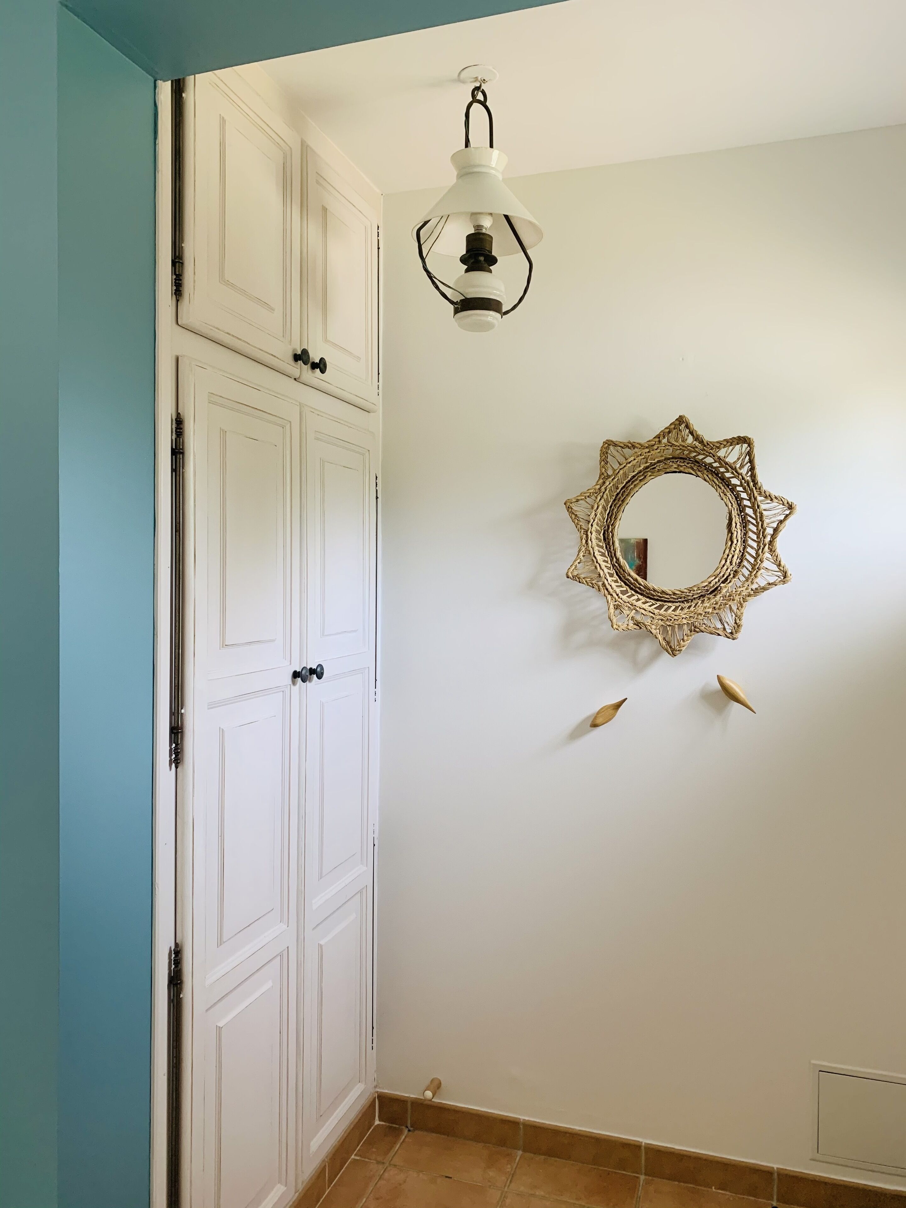 A room with a white door, a hanging light fixture, and a decorative mirror on the wall.