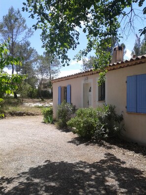 A small house with a gravel driveway, surrounded by trees and shrubs.