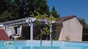 Une piscine aux eaux cristallines, agrémentée d’une pergola, avec un bâtiment visible au fond.