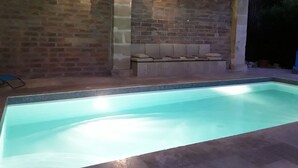 A swimming pool with a tiled edge, a brick wall, and a bench with cushions.