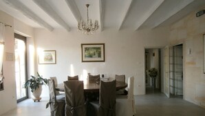 A dining room with a chandelier, a dining table, and chairs. There is a potted plant and a framed picture on the wall.