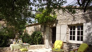 A stone building with a courtyard, featuring a table and two wicker chairs with cushions. - Air-conditioned detached house with a pool, on a family-owned property (Gordes)