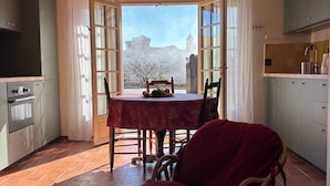 A dining area with a table and chairs, a red chair, a wooden table, a patterned rug, and a view of a building through open doors. - Air-conditioned detached house with a pool, on a family-owned property (Gordes)