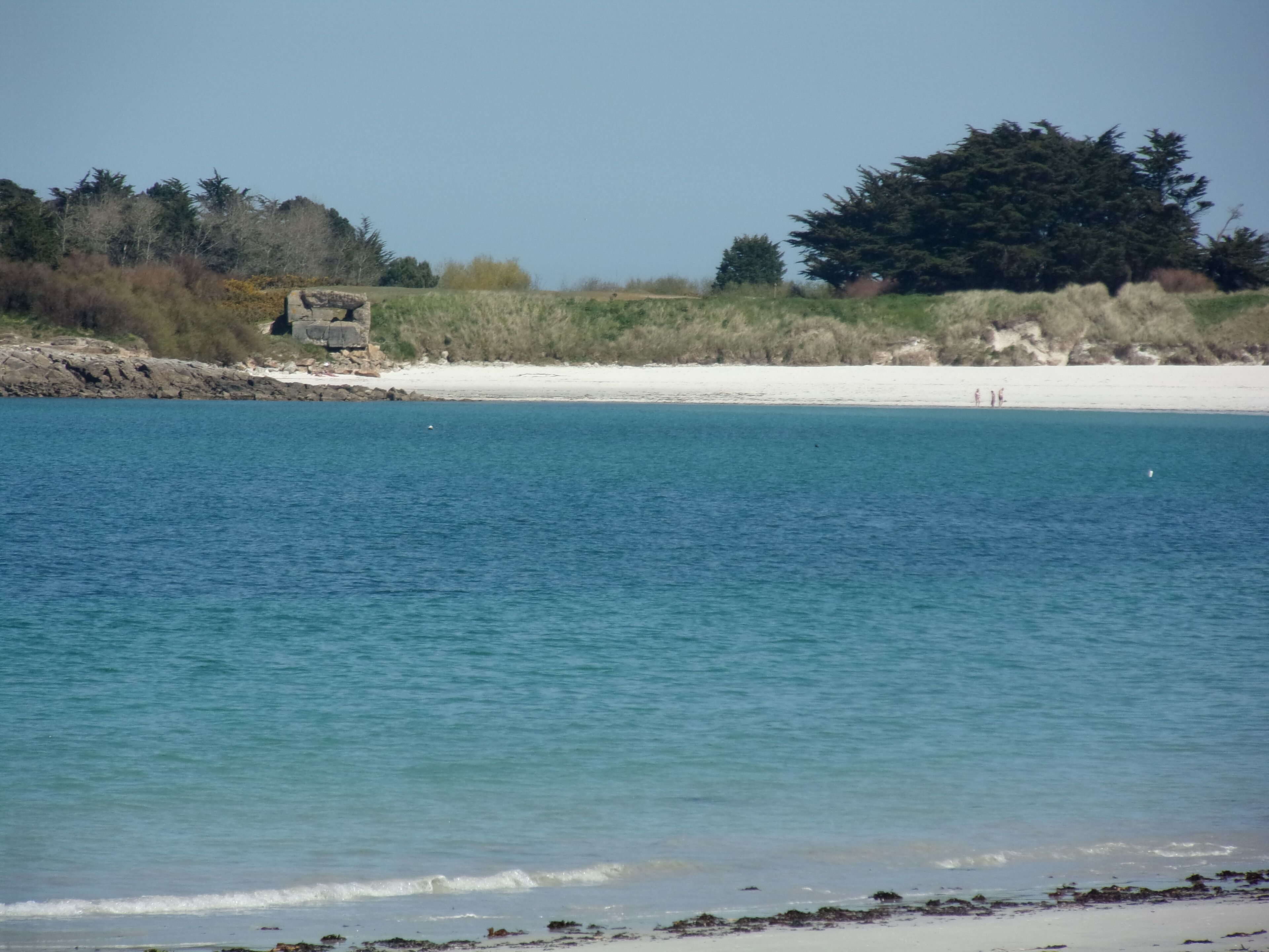 A coastal landscape with a sandy beach, calm sea, and rocky outcrops.