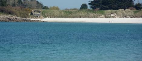 A coastal landscape with a sandy beach, calm sea, and rocky outcrops.