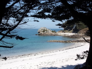 A beach with clear blue water, a rocky outcrop, and a sandy shore.