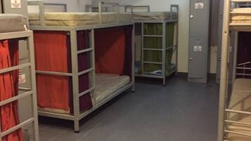 A dormitory room with bunk beds, a green wall, and a tiled floor.