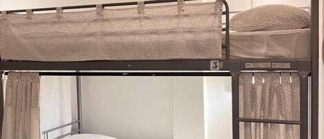 Una cama litera con cabecera, una ventana con cortina y una lámpara de pared.