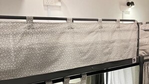 Un lit superposé avec un rideau à motifs, une prise de courant et un luminaire fixé au mur.