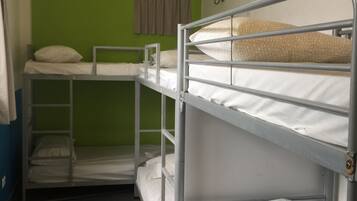 Un dormitorio tipo litera con tres literas, una pared verde, una lámpara colgante y una ventana con cortinas.