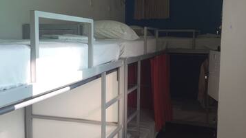 A dormitory room with bunk beds, a desk, a chair, a hanging light fixture, and a wardrobe.