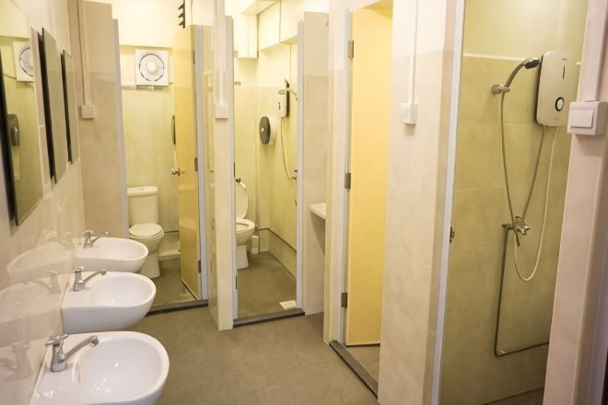 A bathroom with three sinks, a shower, and a toilet.