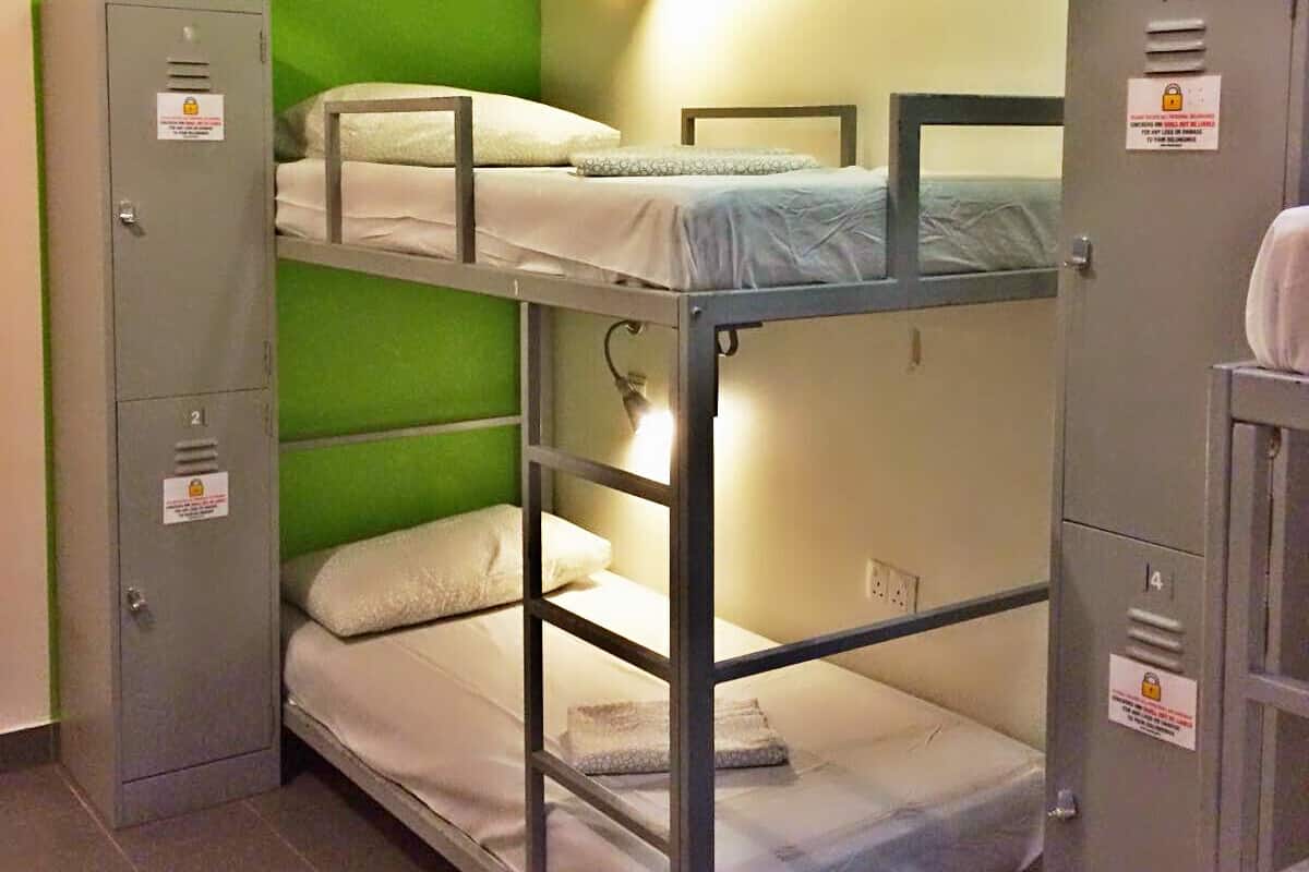 A bunk room with two bunk beds, a green wall, and a light fixture. There are two metal lockers and a door with a lock.