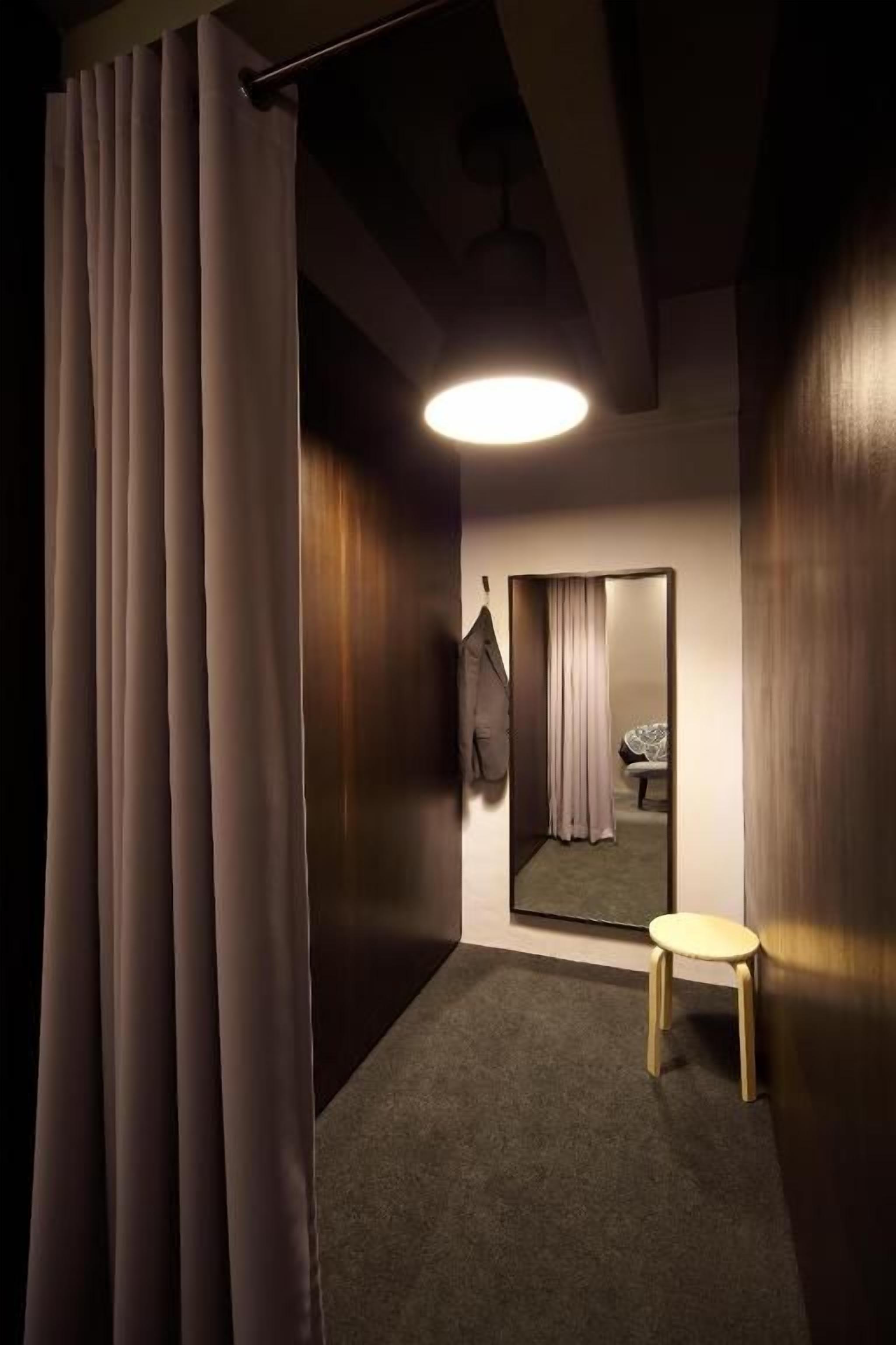 A room with a mirror, a small stool, and a hanging coat.