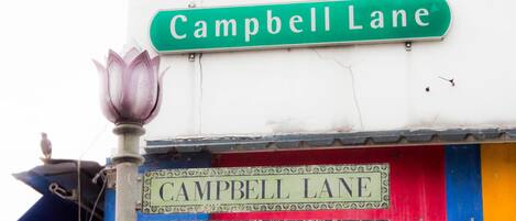 Una señal de calle para Campbell Lane con un farol decorativo y señalización en varios idiomas.