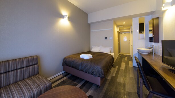 Quarto de hotel com cama, área de estar, escrivaninha com computador e banheiro.