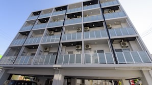 Um edifício com vários andares, varandas, aparelhos de ar condicionado e entrada de garagem.
