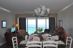 Quarto de hotel com área de refeições, um conjunto de sofás, um candelabro e vista para o mar.