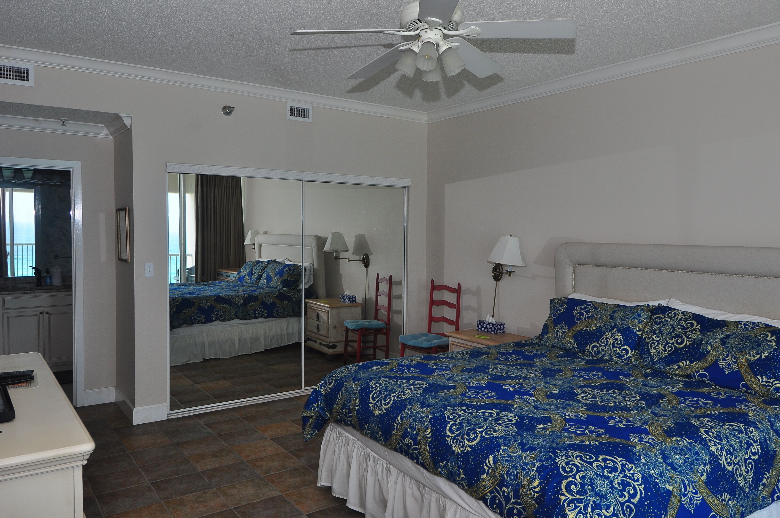 A bedroom with a large bed, a mirror, a ceiling fan, and a dresser.