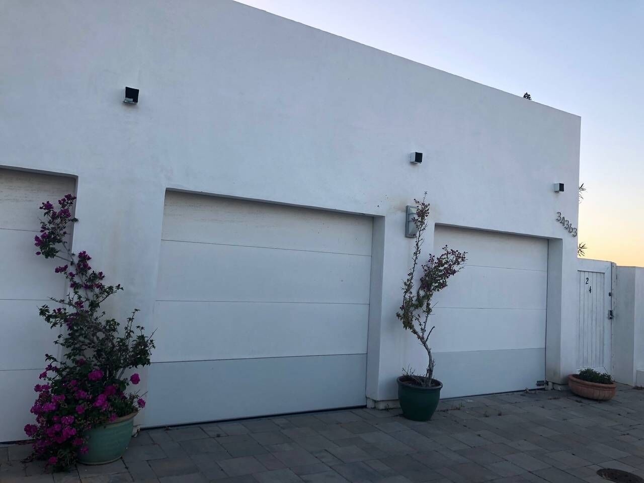 A modern building with two garage doors, potted plants, and a clear sky.