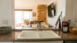 A kitchen with a granite countertop, a double sink, a stone accent wall, a flat-screen TV, and a coffee maker. - Stunning Multimillion Dollar Whitewater -interior by Artist- special 2026 prices (Dana Point)