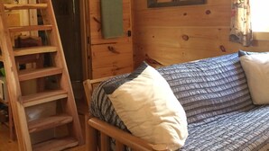 A wooden cabin interior with a loft bed, a ladder, a painting, and a sofa with cushions. - The Lily Pad, headwaters of Eden Falls (Ponca)