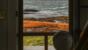 Une vue à travers une porte donnant sur un paysage côtier avec des vagues, des rochers et de l’herbe.