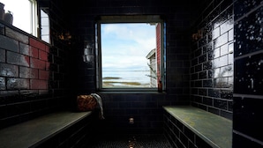 Une petite salle de bain aux carreaux sombres, avec une fenêtre donnant sur la mer.
