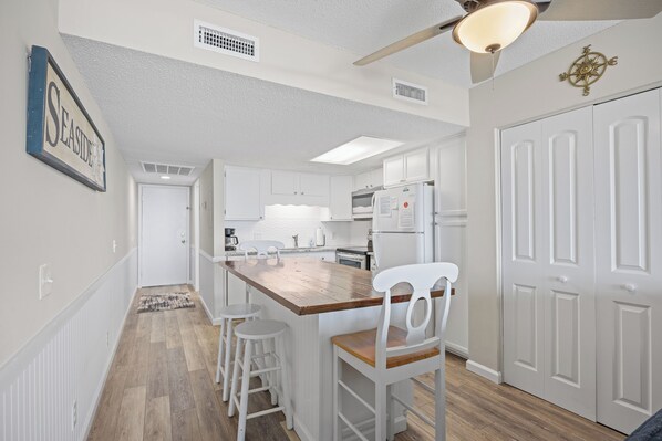 A kitchen with white cabinets, a wooden island, and white bar stools.